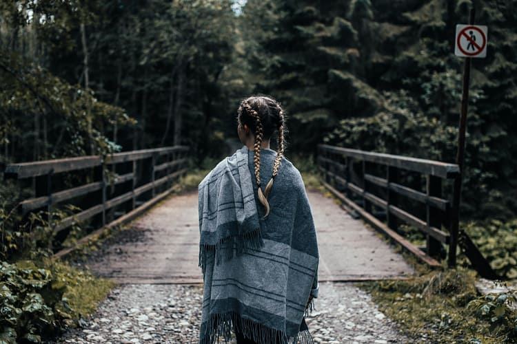 woman in gray shawl standing on forest bridge
